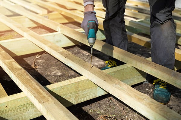 A person using a drill to secure two pieces of wood together on a deck construction project.